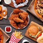A table filled with burgers, fries, chicken, and drinks from the best fast food restaurants.